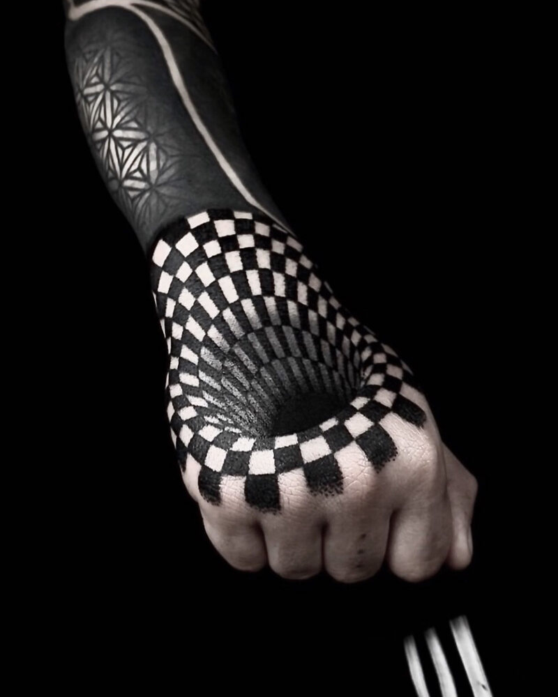 Tatuaje de ilusión óptica en la mano con patrón de damero que simula un agujero, en negro