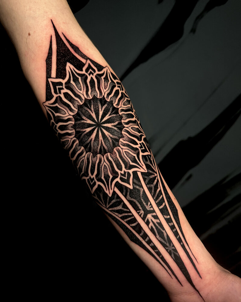 Tatuaje de mandala geométrico con bloques de negro sólido en el antebrazo