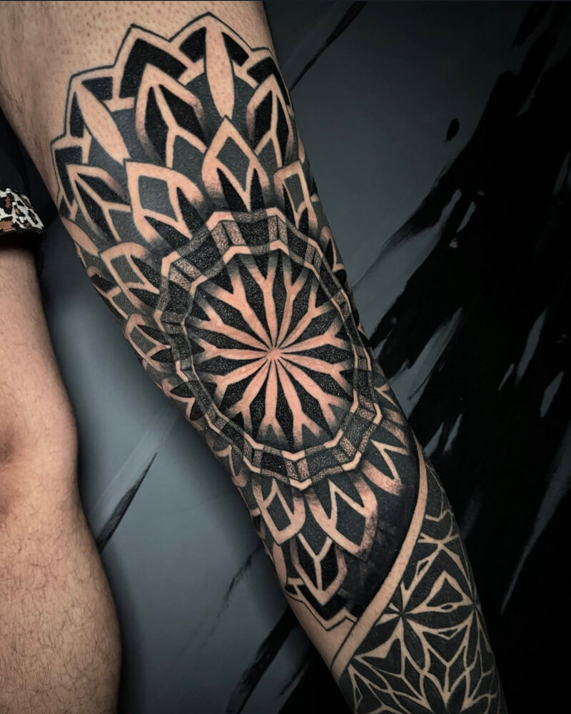 Tatuaje de mandala geométrico con negro sólido en el codo y antebrazo