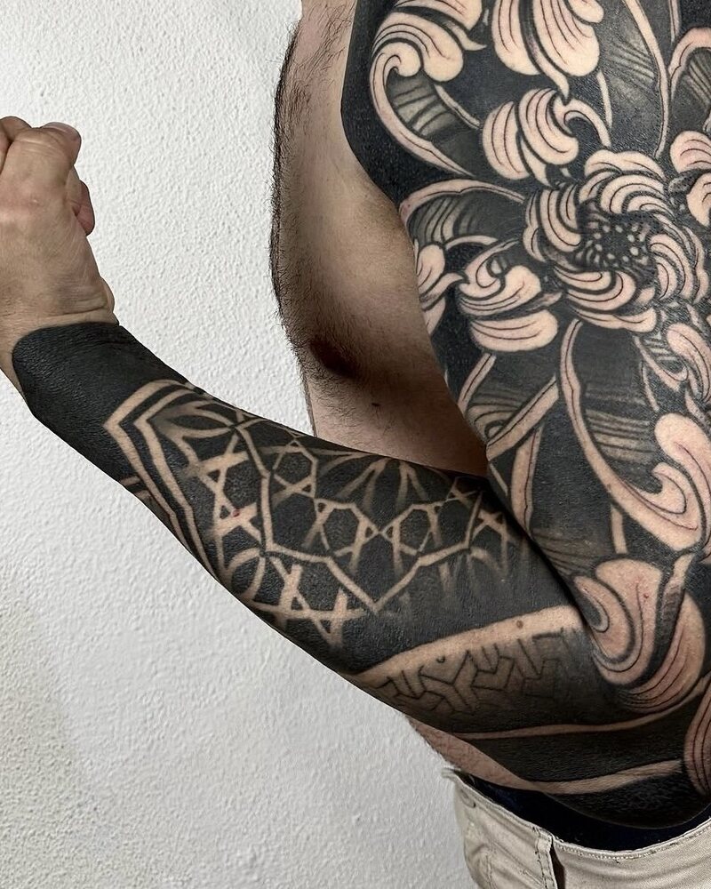Tatuaje blackout de manga completa con una flor grande en el hombro y geometría en el antebrazo, en negro