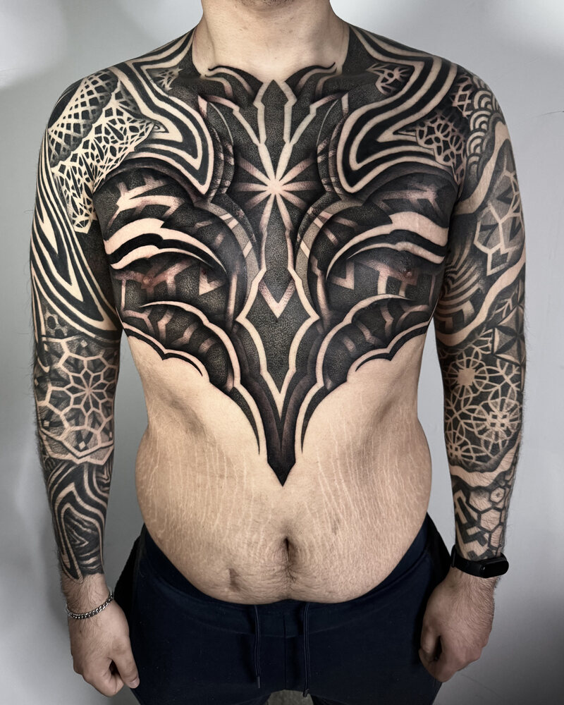 Tatuaje de pechera y mangas con geometría y negro sólido en pecho, hombros y brazos