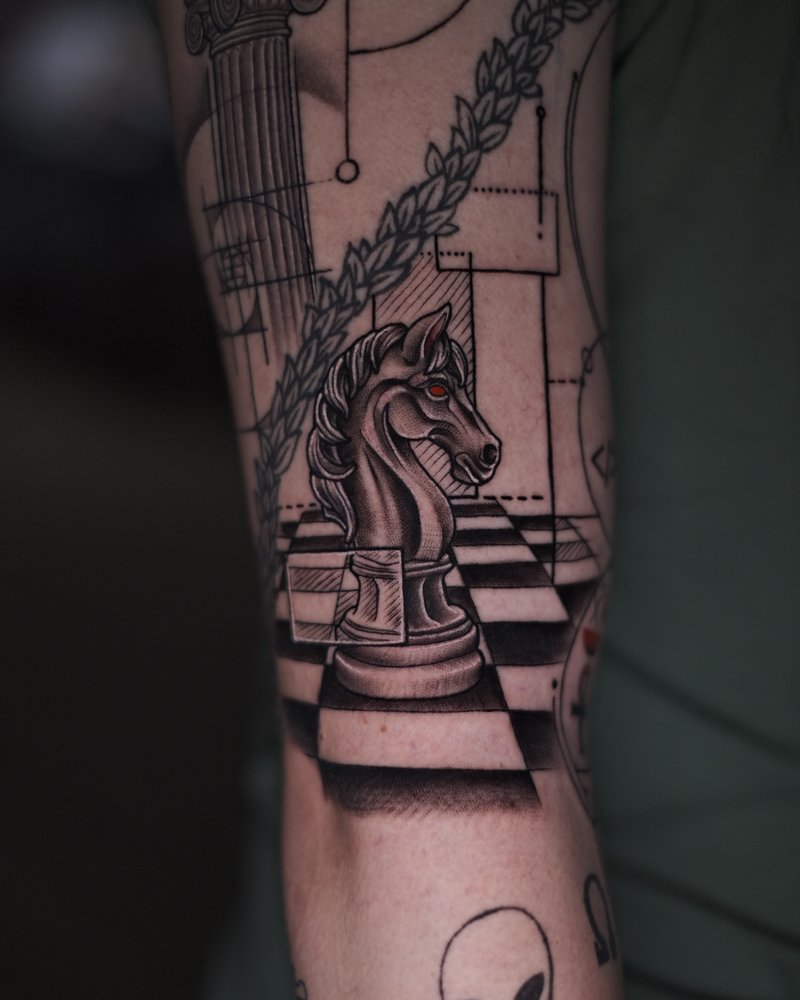 Tatuaje de un tablero de ajedrez con un caballo y una cabeza de alien, en el antebrazo