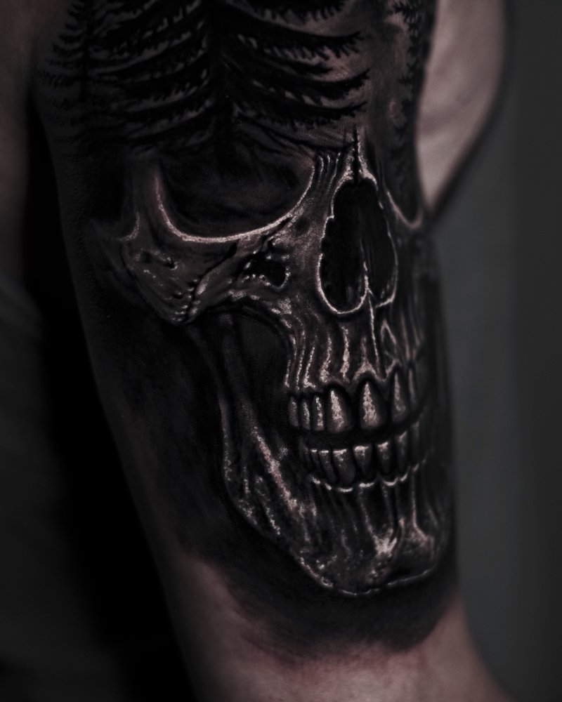 Tatuaje en negro y gris de una calavera con caja torácica, en el brazo