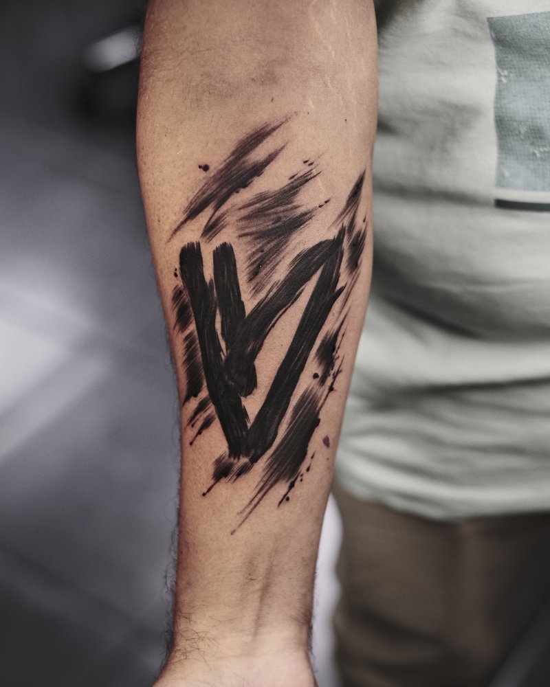 Tatuaje de una letra M con salpicaduras de tinta, en el antebrazo