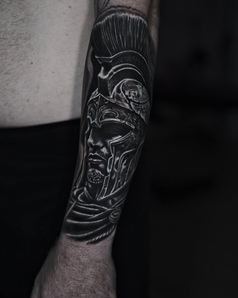 Tatuaje en negro y gris de una máscara con una calavera y un globo terráqueo, en el antebrazo