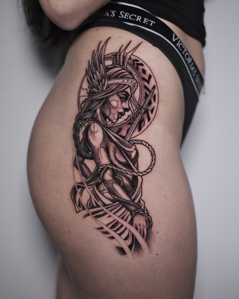 Tatuaje en negro y gris de una figura femenina con una serpiente, en la cadera