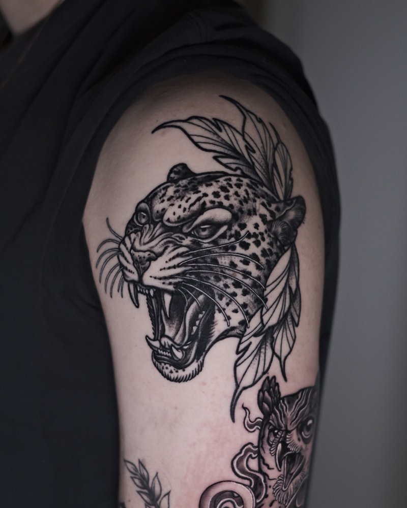 Tatuaje en negro y gris de una pantera con flores, en el brazo
