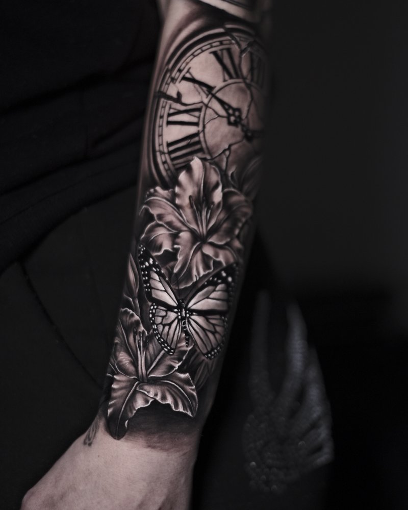 Tatuaje en negro y gris en el antebrazo: reloj agrietado, flor y mariposa