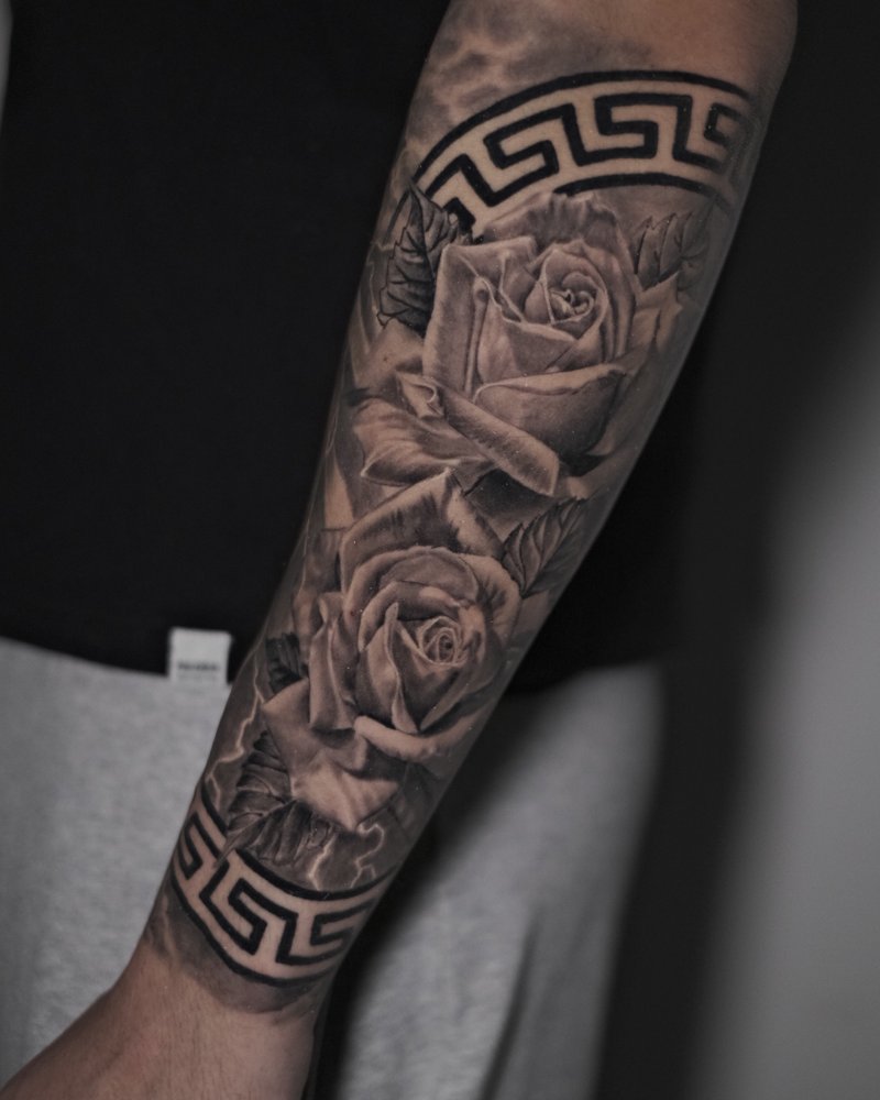 Tatuaje de rosas enmarcadas con una greca griega, en el antebrazo