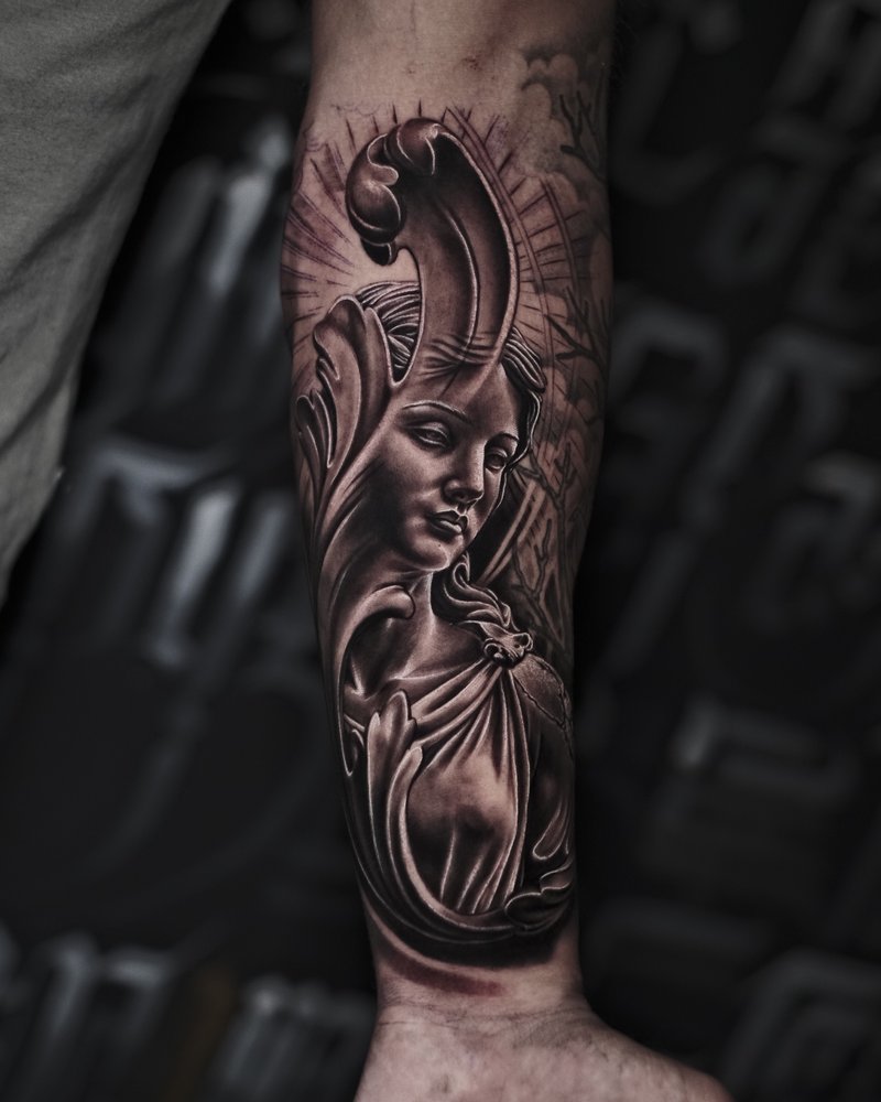 Tatuaje en negro y gris de un rostro con cuernos y serpientes, en el antebrazo