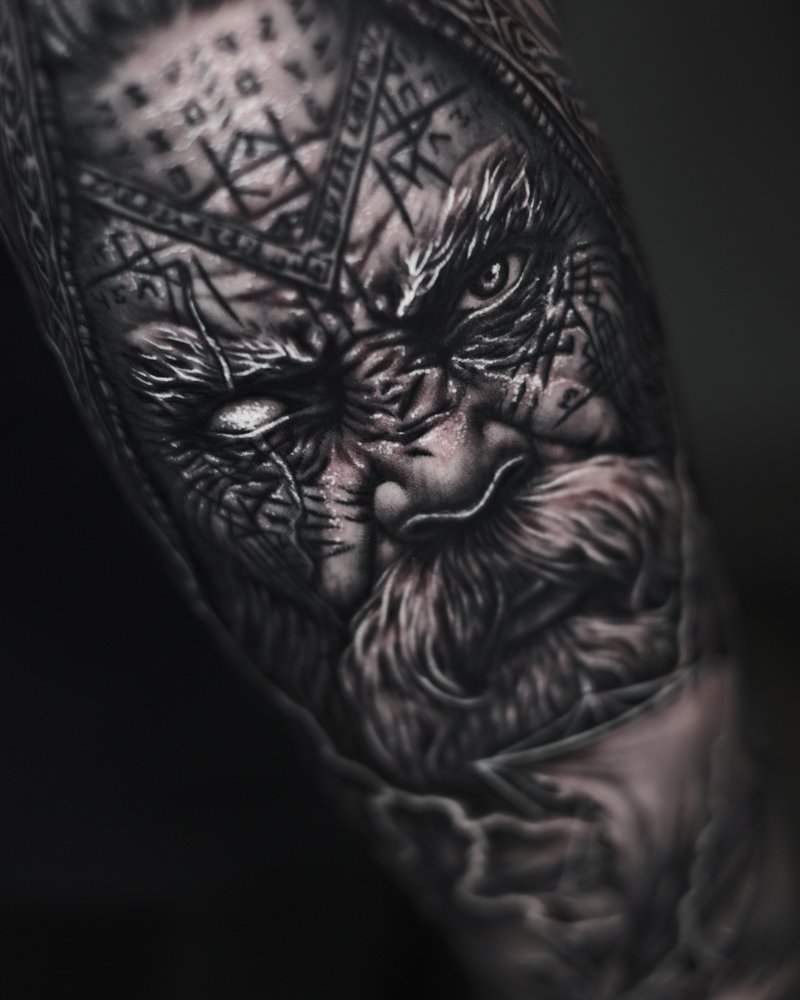 Tatuaje en negro y gris de un rostro con un patrón geométrico, en el antebrazo
