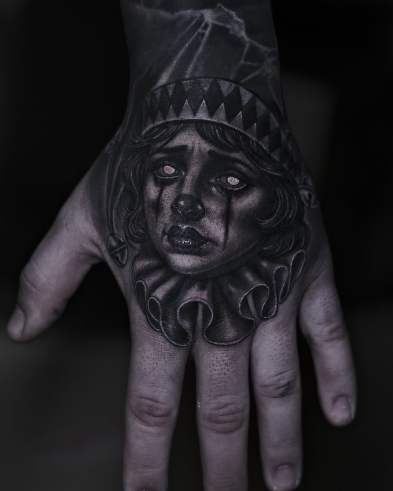 Tatuaje en negro y gris de un rostro con un marco en el dorso de la mano