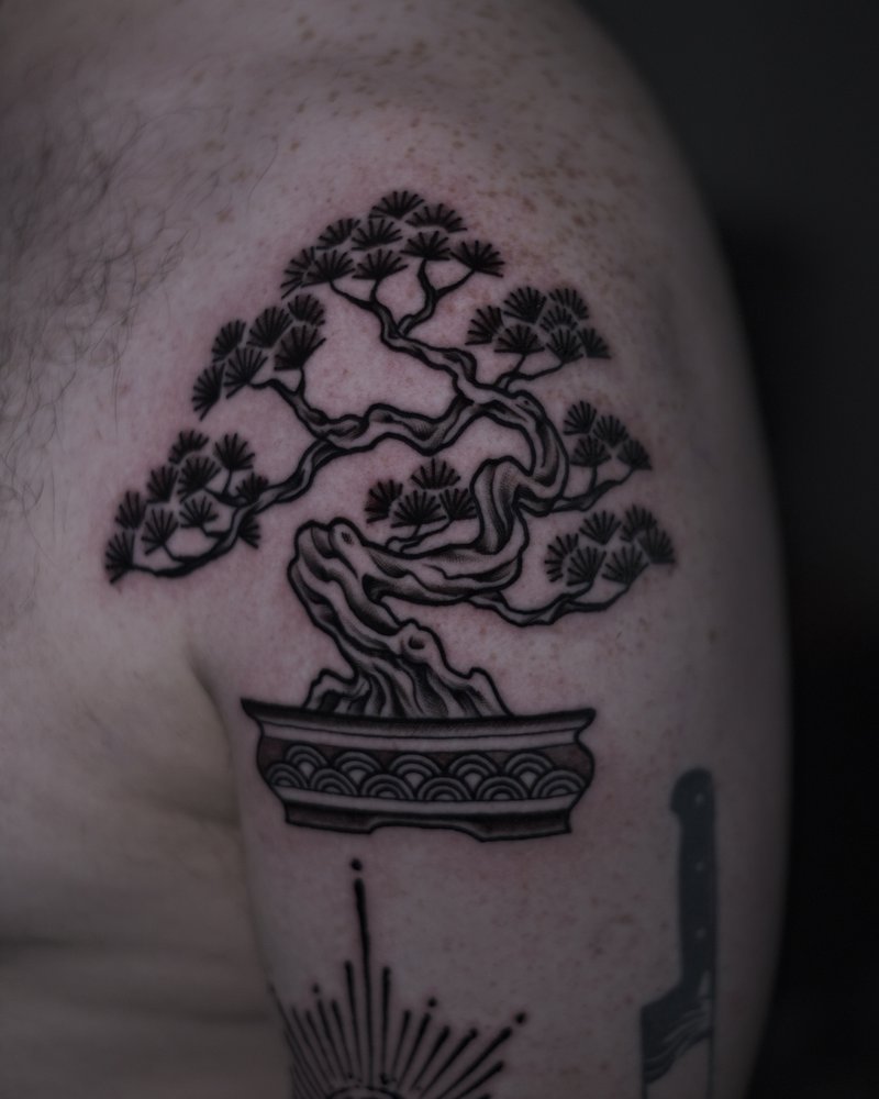 Tatuaje de un bonsai con un sol radiante y un ojo, en el brazo