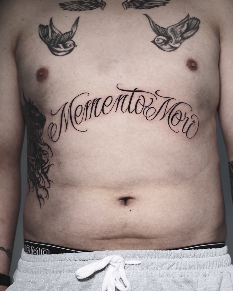 Tatuaje de lettering Memento mori con dos golondrinas en el pecho