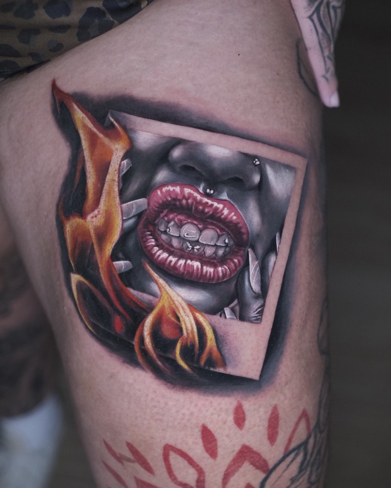 Tatuaje a color de unos labios entre llamas, en el brazo