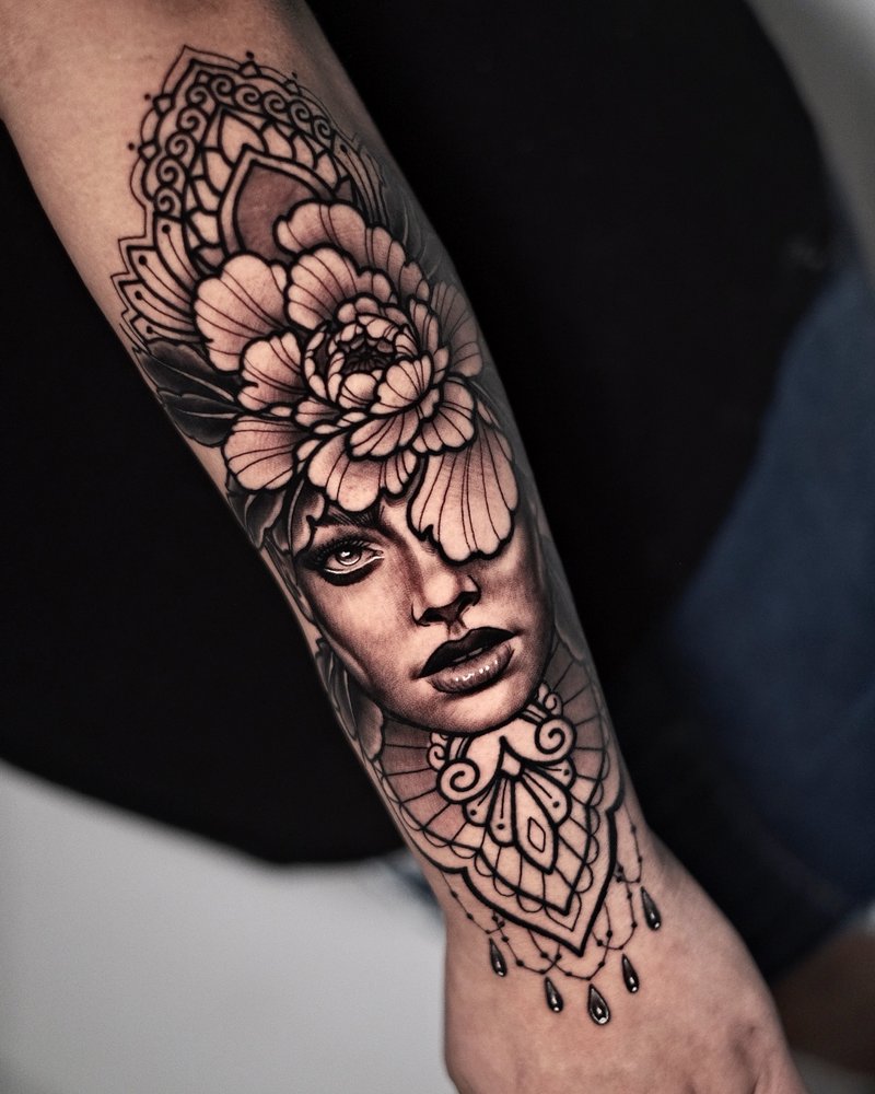Tatuaje en negro y gris de un rostro femenino con una peonía y un farolillo, en el antebrazo