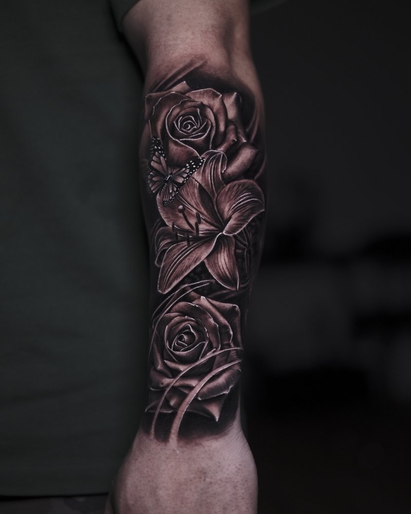 Tatuaje de rosas en negro y gris con un toque de rojo, en el antebrazo